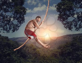 Happy savage flying in the air by rope in the forest at night