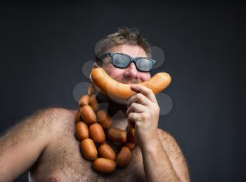 Hungry man with sausages round his neck eats one more sausage over grey