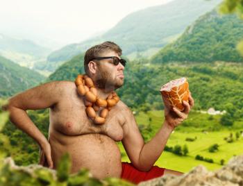 Hungry man with sausages round his neck eats one more sausage in the mountains