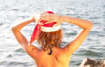 Tan woman in christmas hat looking at the sea