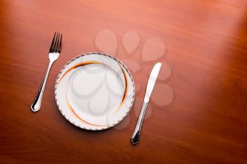 White plate, knife and fork on wooden background