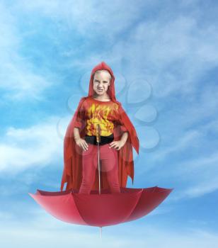 Little girl superhero standing in the umbrella in the sky