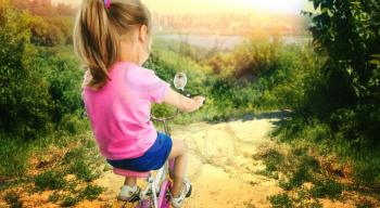 Cute little girl cycling on pink bike in the forest