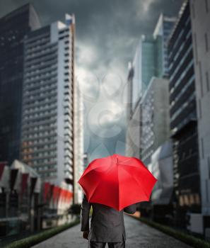 Businessman is standing back with a red umbrella in the city