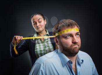 Businesswoman measuring man's head with metre-stick 