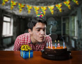 Sad birthday boy smoking in an abandoned room with cake and present