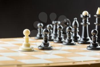 White pawn standing in front of the black chess team