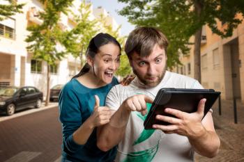 Excited man and woman playing with tablet on the street