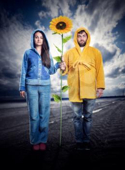 Woman in blue pijama and man in yellow bathrobe holding sunflower outdoor