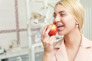 Young woman eating an apple over dentist's office background