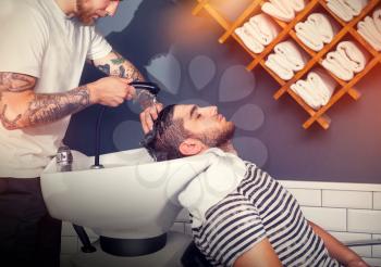 Young man has his hair washed in barber's shop, barber is washing the head of his client