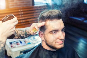 Cheereful young man having hair dress, barber spraying hair with water