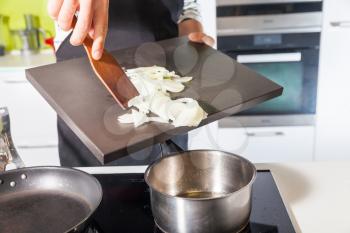 Close up of man's hands putting sliced onion in the pan