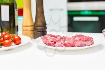 Plate with fresh raw meat stands on a white table