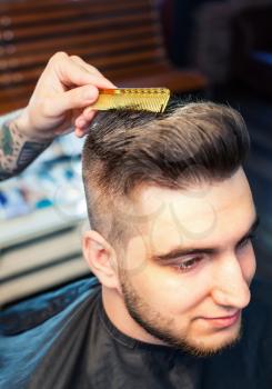 Cheereful young man having hairdress, barber hands combing out