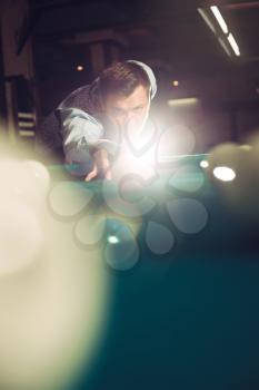 Young man concentrating while playing billiard with light spots