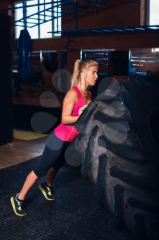 Young girl exercising with a big tire in the gym