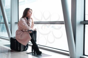 Passenger woman in airport waiting for air travel. Young business woman sitting with travel suitcase in waiting hall of departure lounge in airport