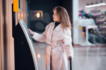 Young woman at self service transfer area doing self-check-in or buying plane tickets in modern airport terminal building