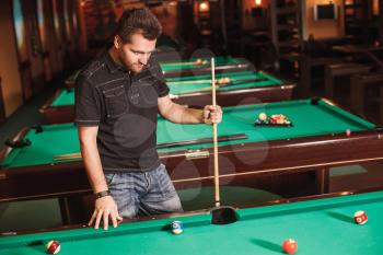 Concentrated player with a cue in billiard room. Playing billiards.