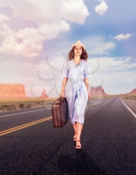 Traveler woman with suitcase, walking on the road. Blue sky with clouds and rocky mountains on the background. Travel concept.