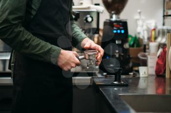 Hands of the man in black apron who prepares the coffee machine
