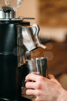 Coffee grinder fills coffee in a cup. Male hand holding a cap near the coffee grinder against blur background.