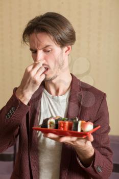 Man holds sushi set with a hand, the second hand closes a nose from a smell