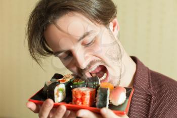 Young man trying to eat sushi set without hands. Traditional japanese food.