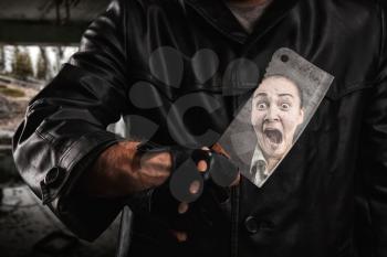 Serial maniac standing under bridge and holding knife in hand, reflection of his horror victim face on a knife blade.