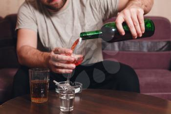 Lonely man drinking behind bottles of alcohol