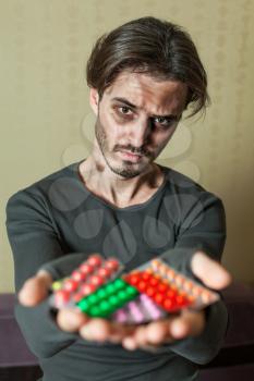 Drugs addict is holding a lot of different tablets in both his hands.