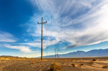 Power lines in desert valley, blue sky with clouds on background.