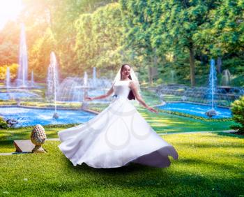 Young bride in white dress, green park with fountains on background