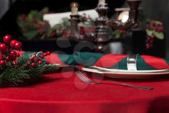 Luxury restaurant interior, rich tableware closeup. Table covered with a red cloth, candlestick and pine branches decoration