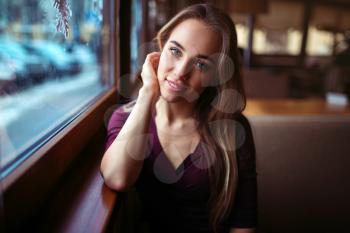 Woman waiting in cafe. Young girl sitting against the window and waiting for the order in restaurant.