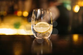 Beverage with slice of lemon and ice cubes on wooden bar counter