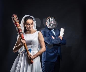 Newlyweds serial murderers with bloody bat and meat cleaver, black background. Groom in hockey mask