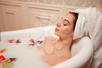 Beautiful woman in bathroom with rose petals and foam.