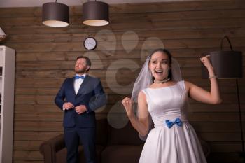Portrait of happy bride and serious groom, wooden room on background.