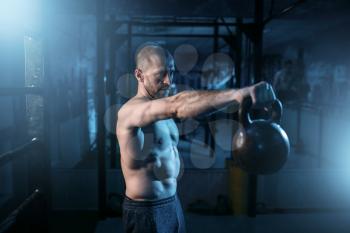 Muscular man exercises with kettlebell on training in gym. Strong athlete workout with weight