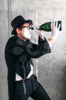 Pantomime theater actor performing with big bottle. Comedy mime artist in suit, gloves, glasses, make-up mask and hat