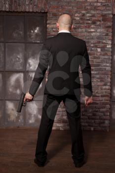 Contract murderer with gun wallpaper concept, back view. Bald assassin in suit holds weapon in hand. Secret agent on mission