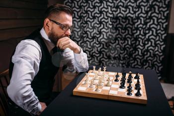 Pensive male chess player in glasses thinking about game strategy. Intelligence competition concept