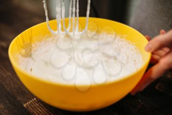 Dough whipping in bowl with a mixer. Sweet cake cooking preparation. Wooden background