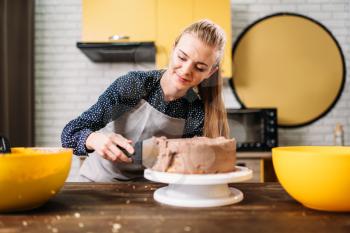 Woman cook smears baked cake with chocolate cream. Tasty dessert preparation. Homemade cooking