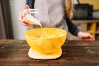 Female hands adds sugar into a bowl with dough on wooden table. Tasty cake cooking preparation