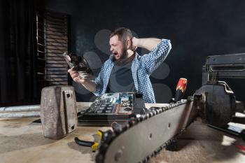 Computer engineer fixing problem with electronic components of hardware. Chainsaw and anvil on the table, engineering humor 
