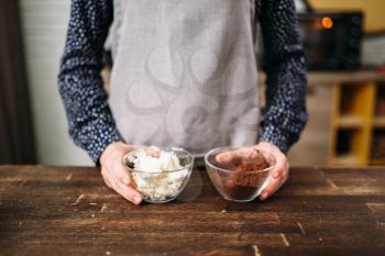 Female hands holds glass bowls with chocolate powder and butter. Sweet dessert cooking preparation