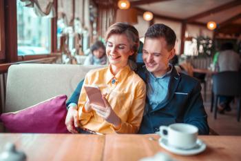 Love couple looks on phone photo album, restaurant on background. Man and woman happy together